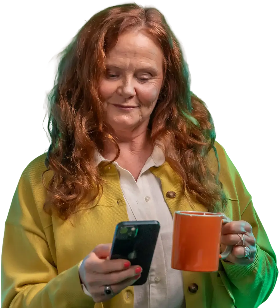 Woman smiling at her phone while holding a mug